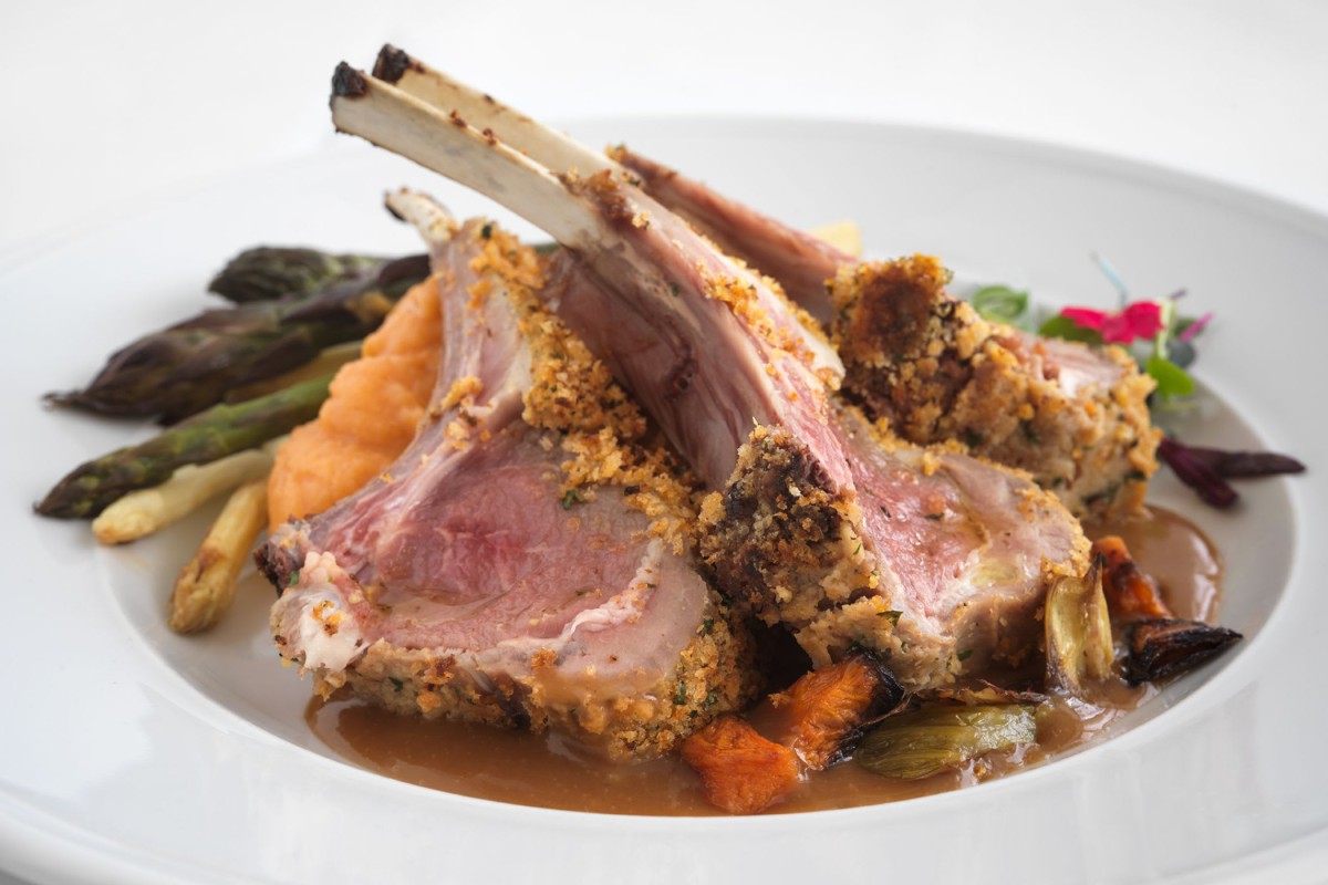 A gourmet rack of lamb served with vegetables.