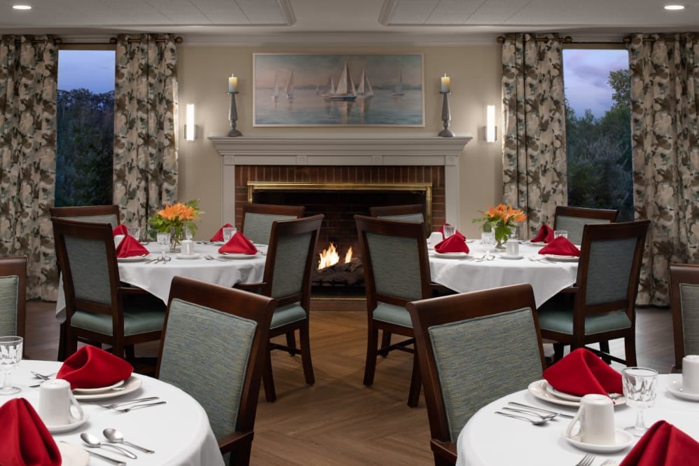 An elegant dining room with round tables set for a formal dinner, featuring a cozy fireplace.