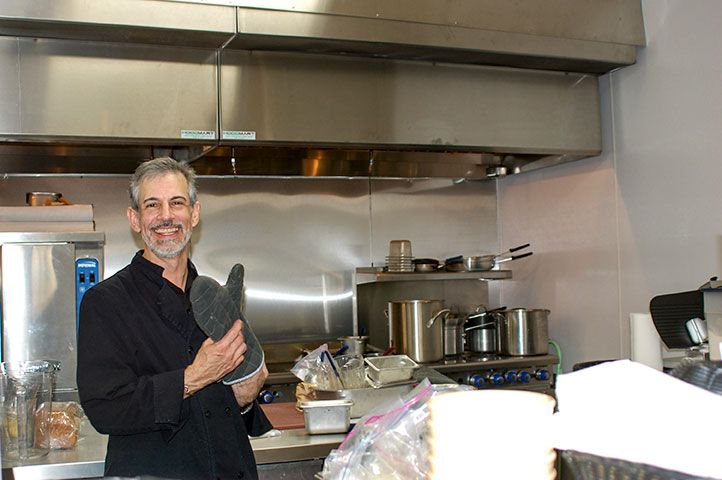 A chef smiling while holding a piece of kitchen equipment in a restaurant kitchen.