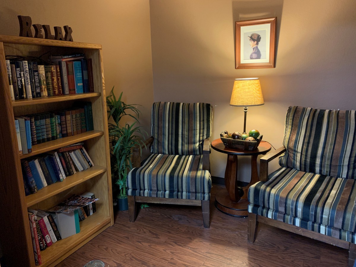 A cozy living room corner featuring two striped chairs, a wooden table with a lamp, and a bookshelf filled with books.