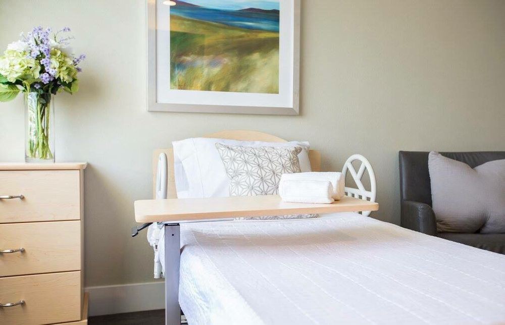 A neatly arranged hospital bed with a side table in a well-lit room featuring modern artwork.