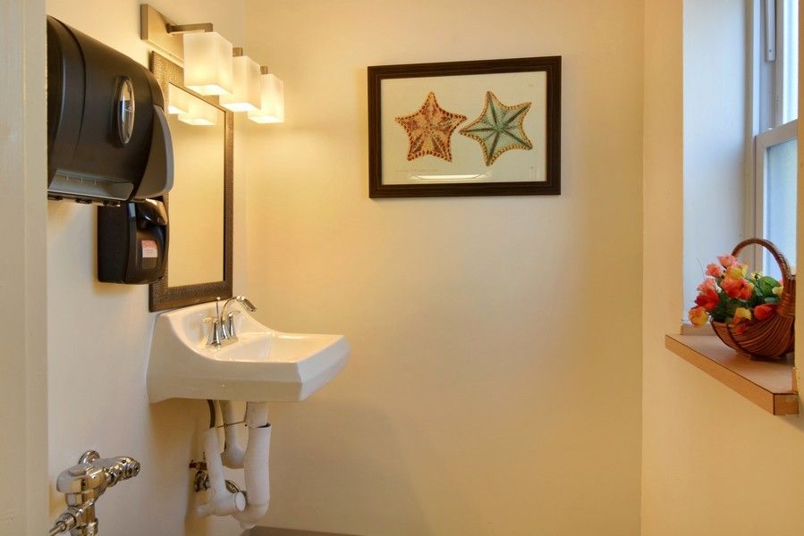 A bathroom interior featuring a sink with a mirror, overhead lighting, and framed starfish artwork on the wall.
