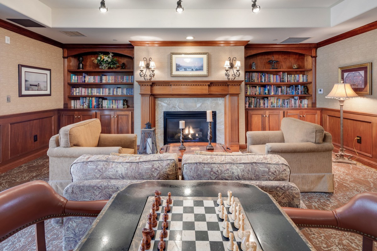 A cozy living room with a fireplace, surrounded by bookshelves and featuring a chess board.