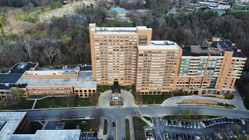 An aerial view of a large residential building surrounded by green trees and a parking area.