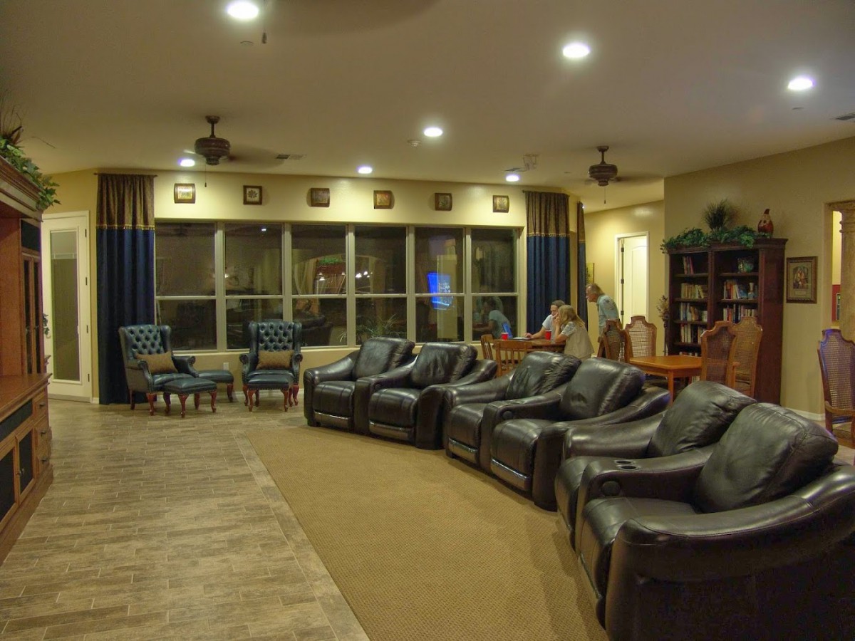 A spacious living room featuring a row of recliner chairs, large windows with curtains, and cozy ambient lighting.