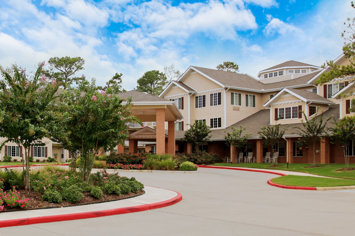 A well-maintained retirement home surrounded by lush landscaping and a clear blue sky.