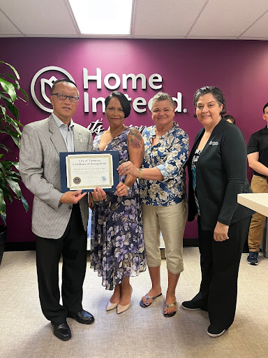 A group of individuals proudly holding a certificate during a recognition event at Home Instead.
