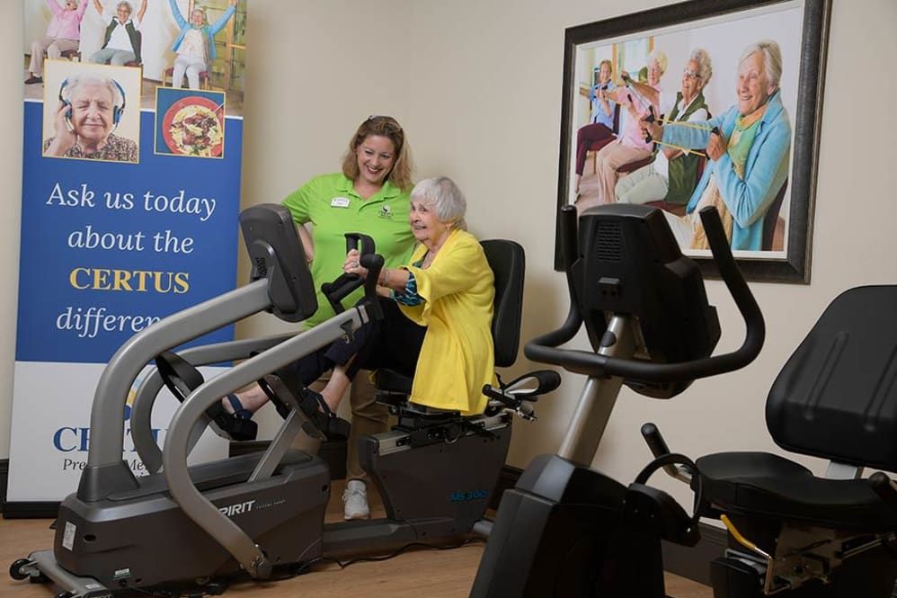 An elderly woman receives guidance from a trainer while using a recumbent bike at a community gym.