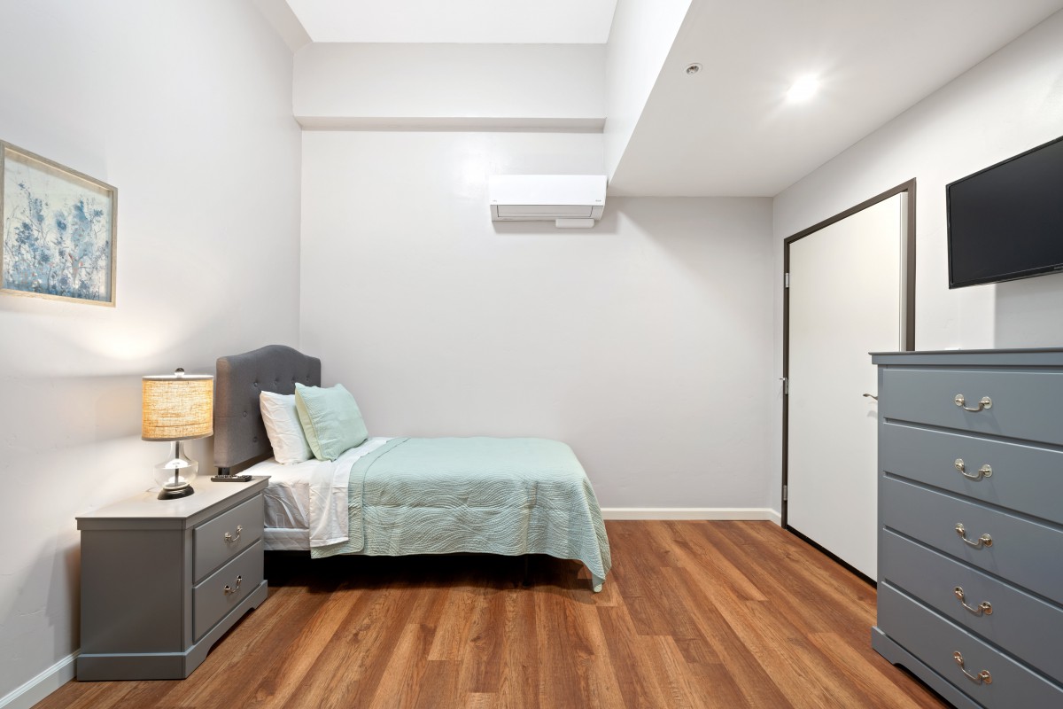 A minimalist bedroom with a bed, nightstand, and hardwood flooring.