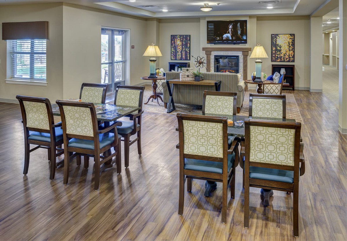 A well-lit dining area with tables and chairs, featuring wooden flooring and decorative artwork.