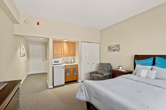 A cozy bedroom with a kitchenette featuring a microwave, refrigerator, and comfortable seating.