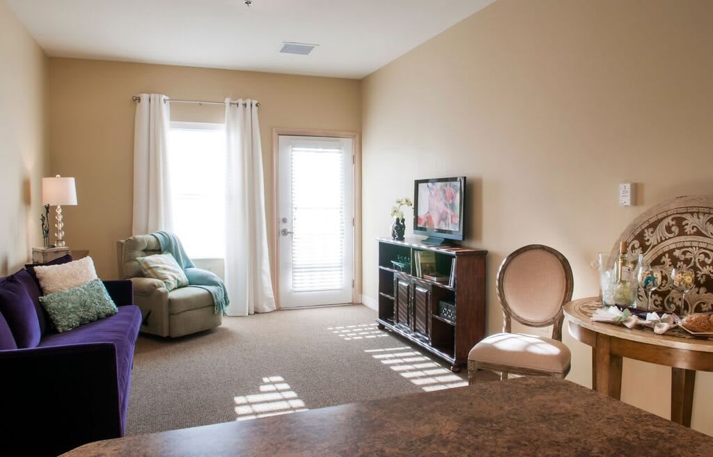 A cozy living room interior with a television, seating, and ample natural light.