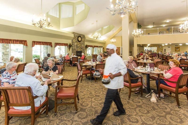 A lively dining area with seniors enjoying a meal, served by attentive staff under elegant chandeliers.