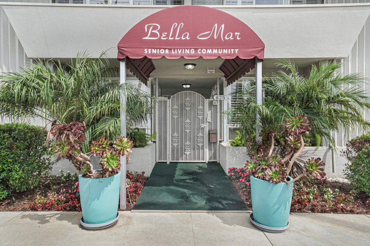 Entrance to 'Bella Mar' apartment with decorative plants and a red awning.