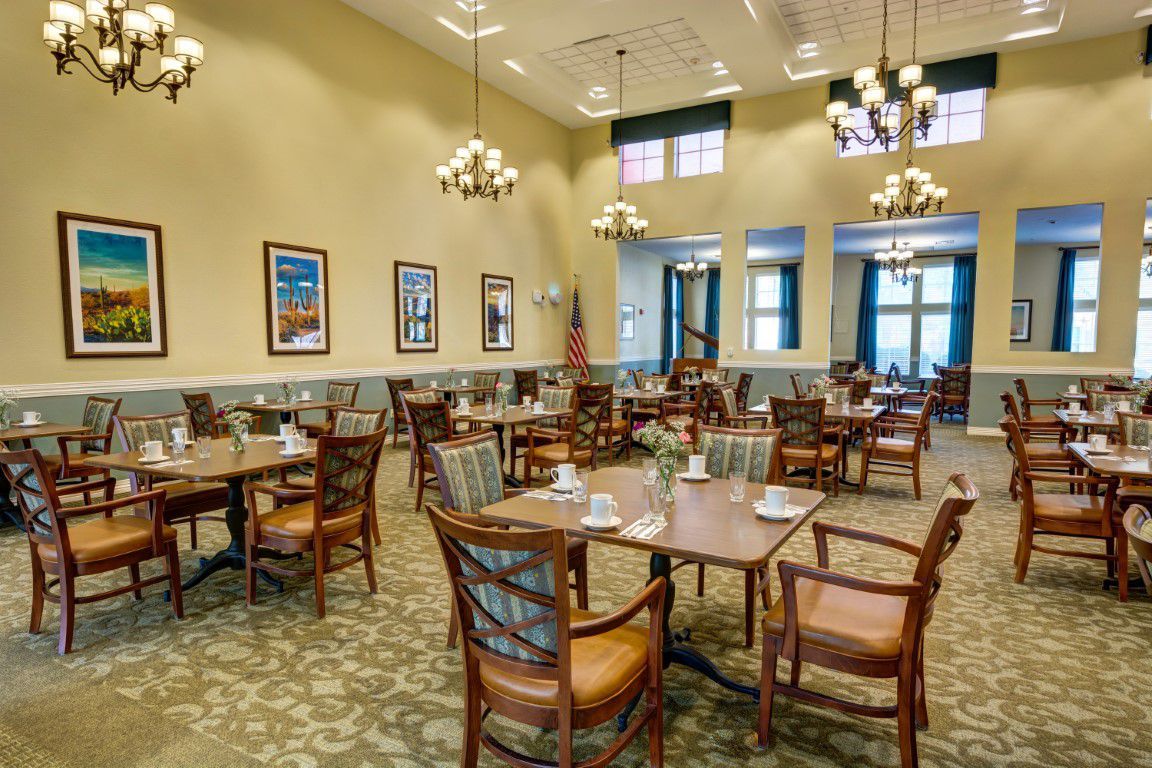 A spacious dining room with neatly arranged tables and chairs, adorned with chandeliers and decorative elements.
