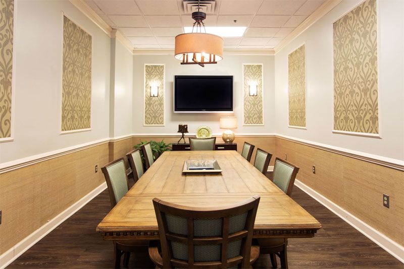 A well-lit conference room with a wooden table, chairs, and a television mounted on the wall.