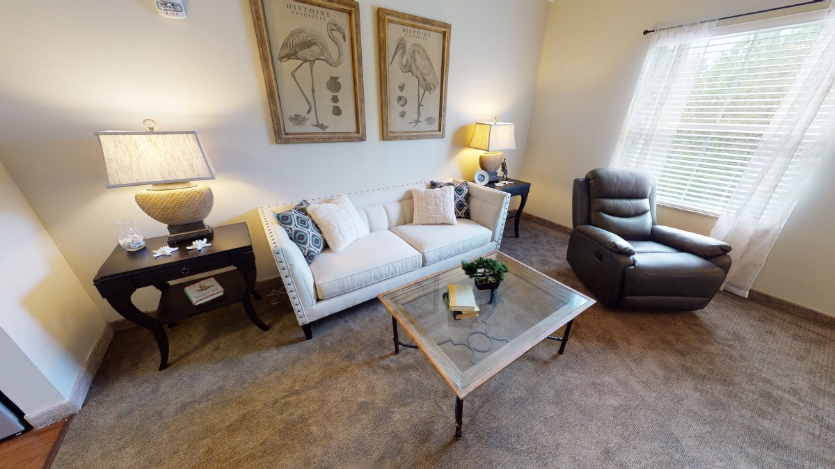 A cozy living room with a sofa, armchair, and coffee table, adorned with flamingo artwork and soft lighting.