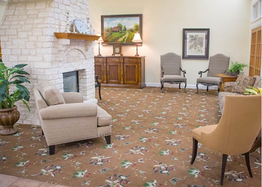 A cozy living room with a fireplace, chairs, and a painting on the wall.