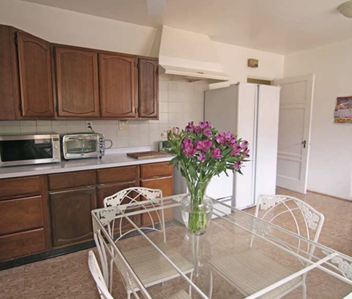 A cozy kitchen with wooden cabinets, a dining table adorned with fresh flowers, and various appliances.