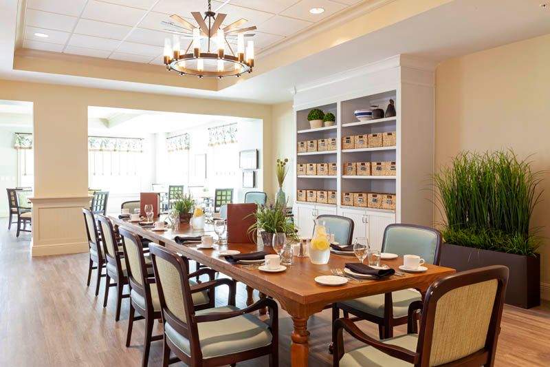 An elegant dining room with a long table, set for a meal, surrounded by upholstered chairs and lit by a chandelier.