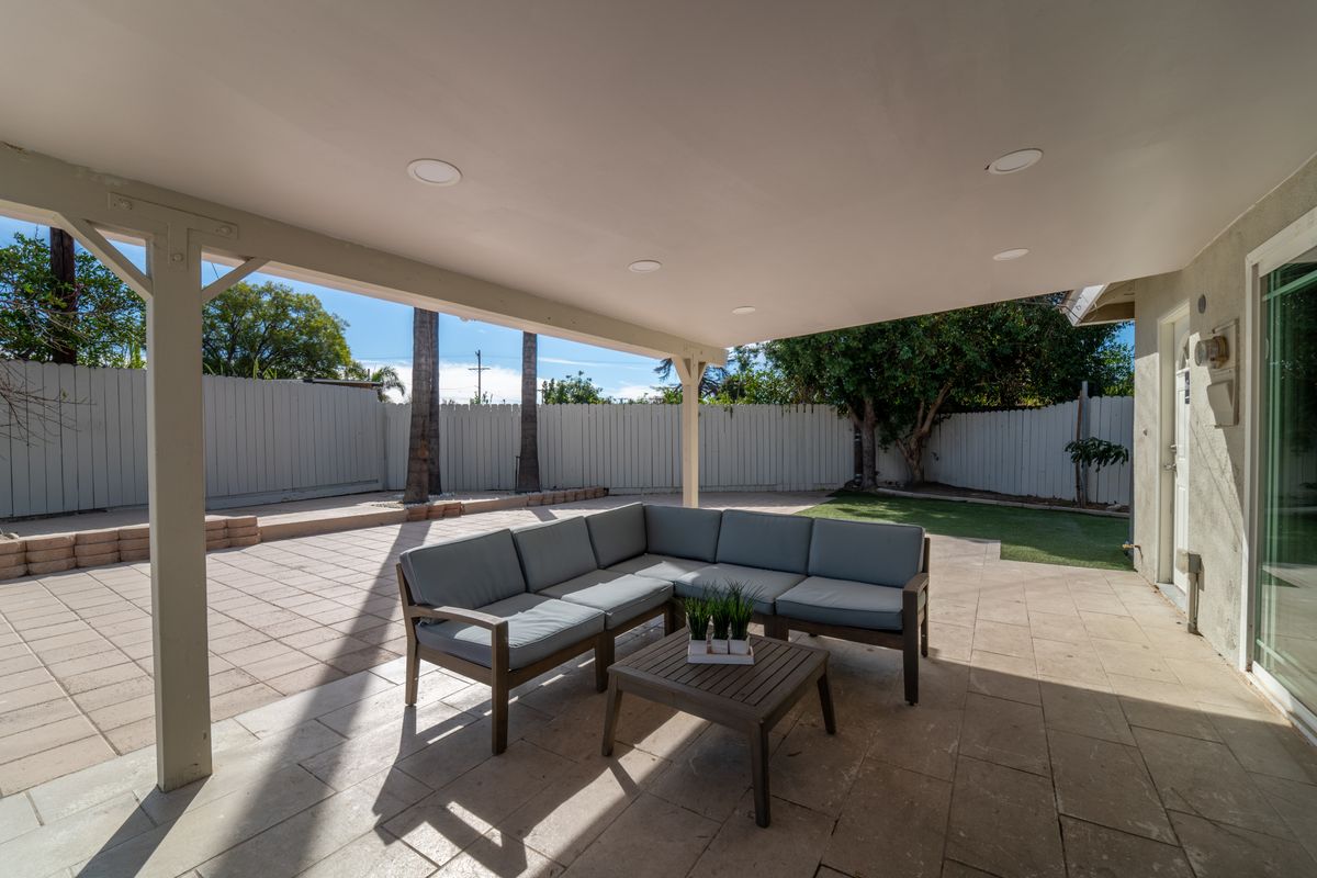 A cozy outdoor patio with a sectional sofa and table under a covered area, surrounded by a spacious backyard.
