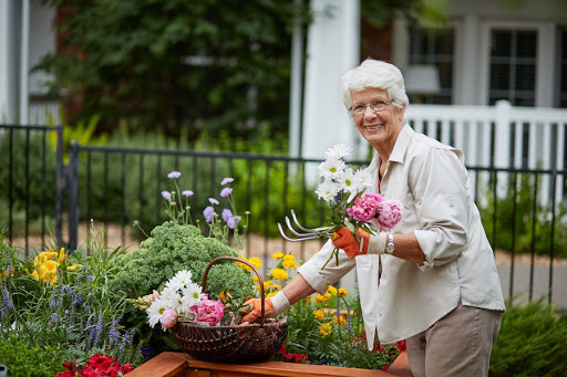 A cheerful woman enjoys her time in the garden, tending to beautiful flowers and gathering them in a woven basket.