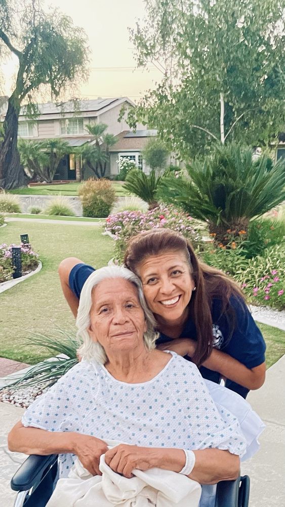 An elderly woman and a younger woman smiling together in a garden.