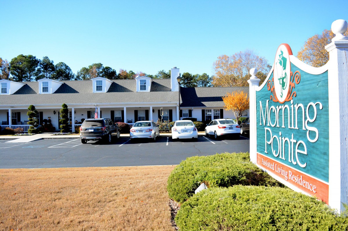 A street view of an office building with a parking lot and sign in the foreground.