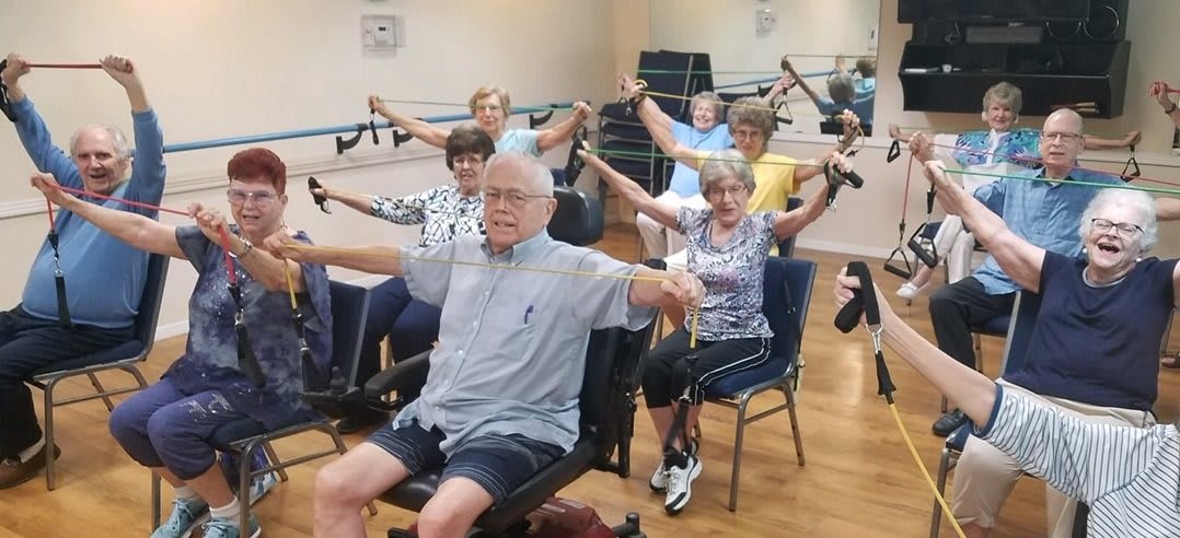 A group of seniors participating in a seated exercise class, using resistance bands.