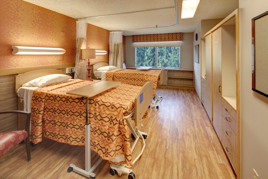 A hospital room with two neatly made beds and a large window providing natural light.