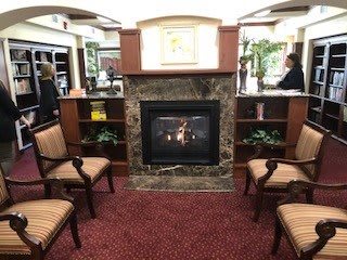Cozy library interior with a central fireplace and upholstered chairs.