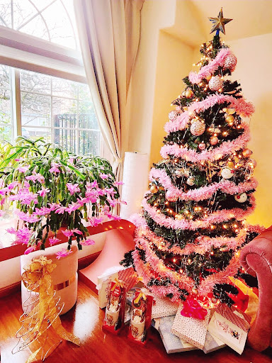 A beautifully decorated Christmas tree adorned with pink tinsel, surrounded by gifts and a lovely indoor plant.