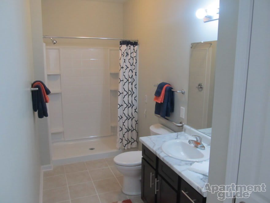 A clean, modern bathroom featuring a shower with a patterned curtain, a sink with a marble countertop, and a toilet.