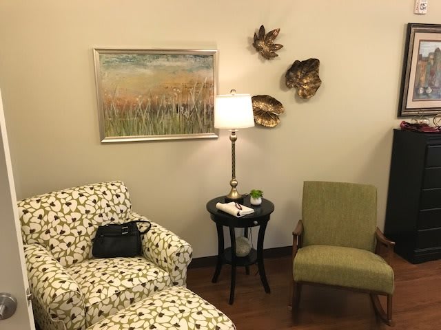 A cozy waiting room with patterned and plain chairs, a side table with a lamp, and decorative wall art.