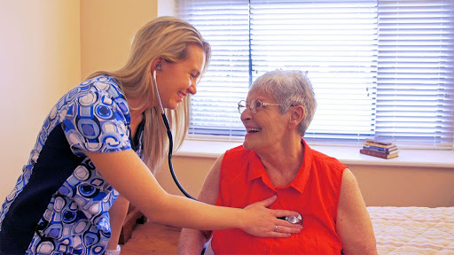A healthcare professional smiles as she checks the heart of an elderly woman using a stethoscope.