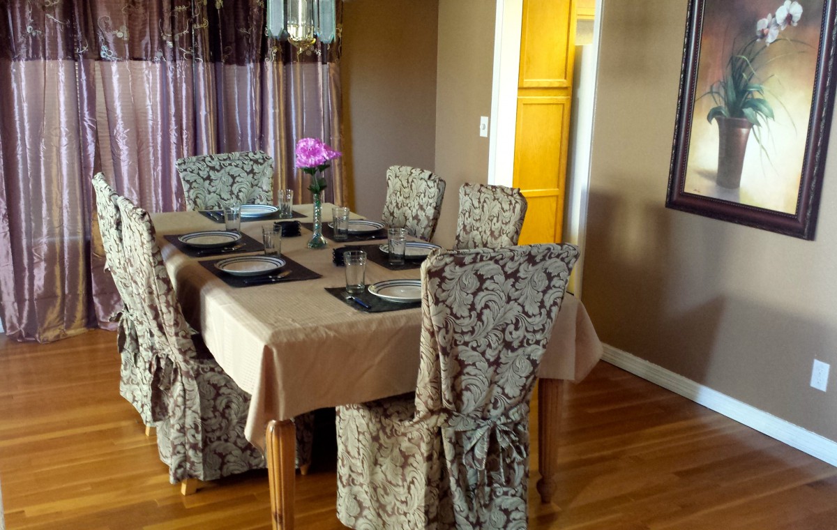 A well-decorated dining room with patterned chair covers, a neatly set table, and a vase of flowers.
