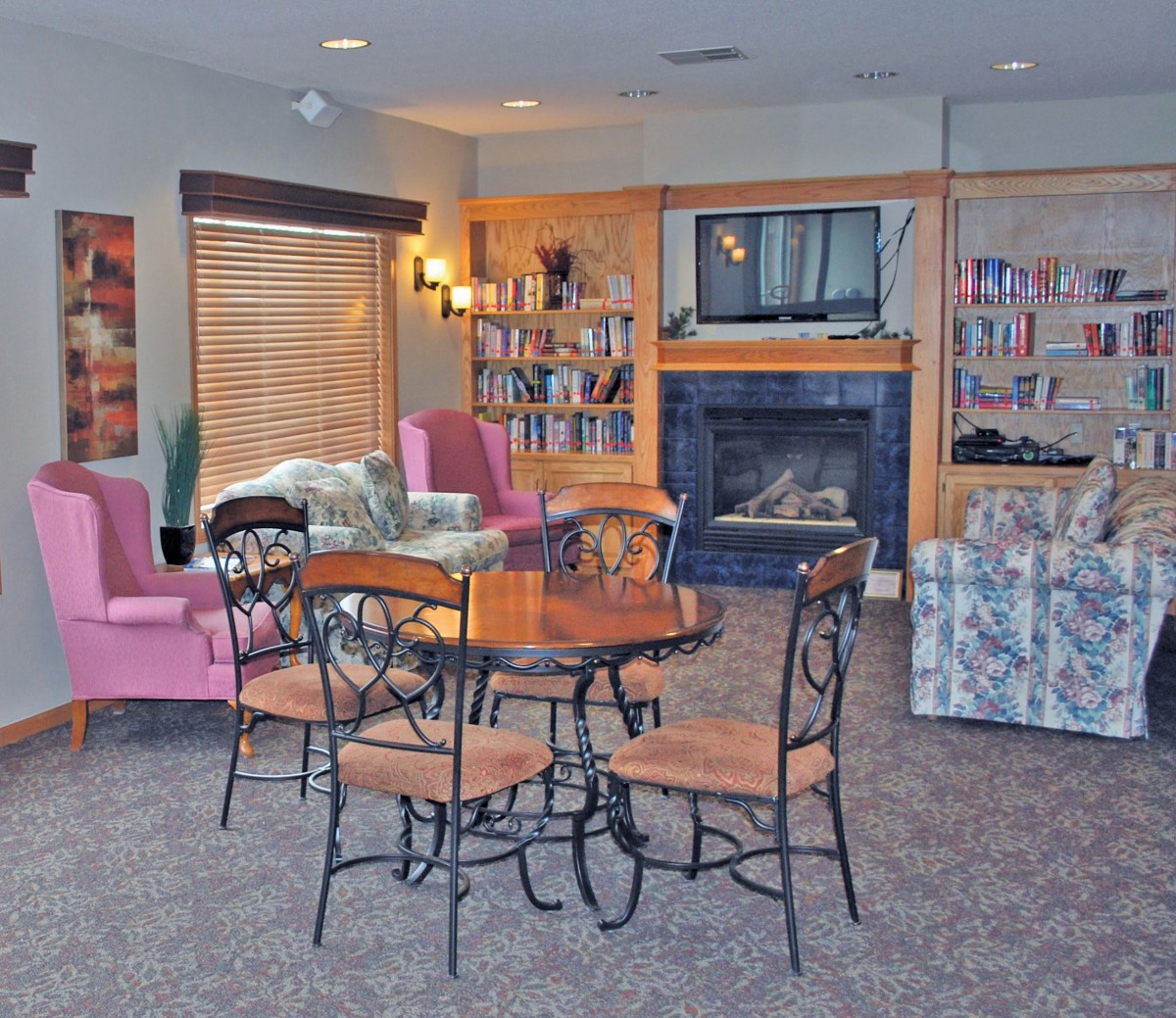 A cozy living room with a seating area, table, and fireplace surrounded by bookshelves.