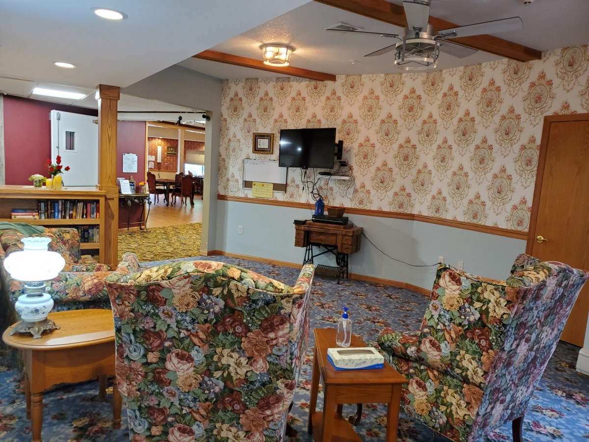A cozy living room with floral-patterned couches and classic wallpaper.