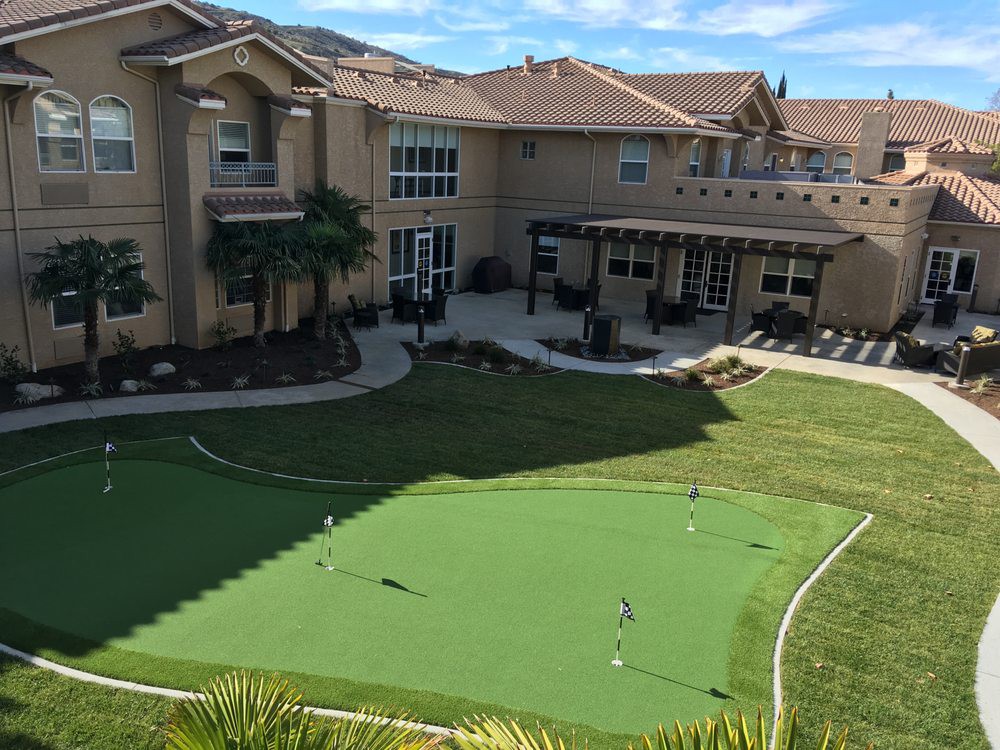 A luxury home with a backyard featuring a golf putting green and patio area.
