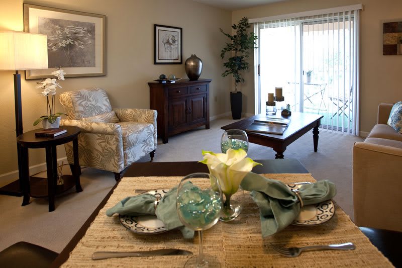 A cozy living room with a dining table set for two, featuring elegant decor and natural lighting.
