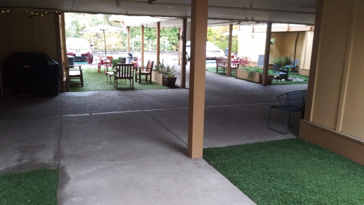 A covered outdoor seating area with chairs and tables surrounded by greenery.