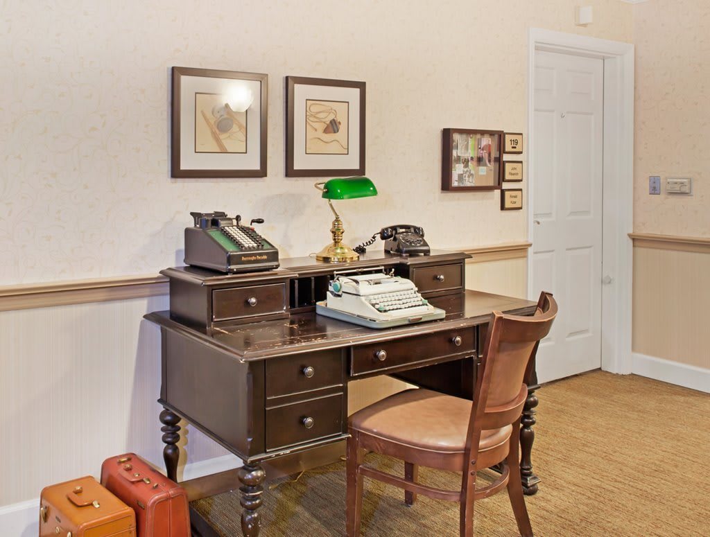 A vintage-style office setup featuring a wooden desk with a typewriter and telephone, surrounded by classic decor.
