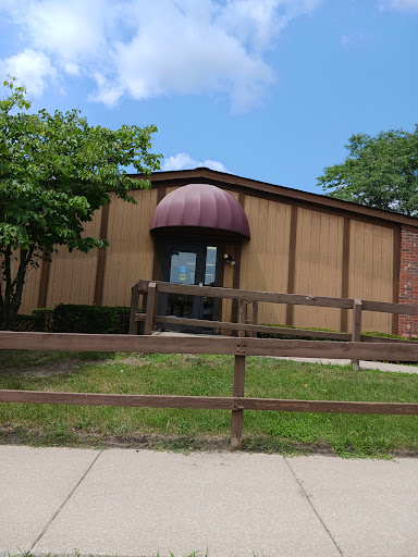A peaceful view of a building with a brown awning, surrounded by greenery and a wooden fence.