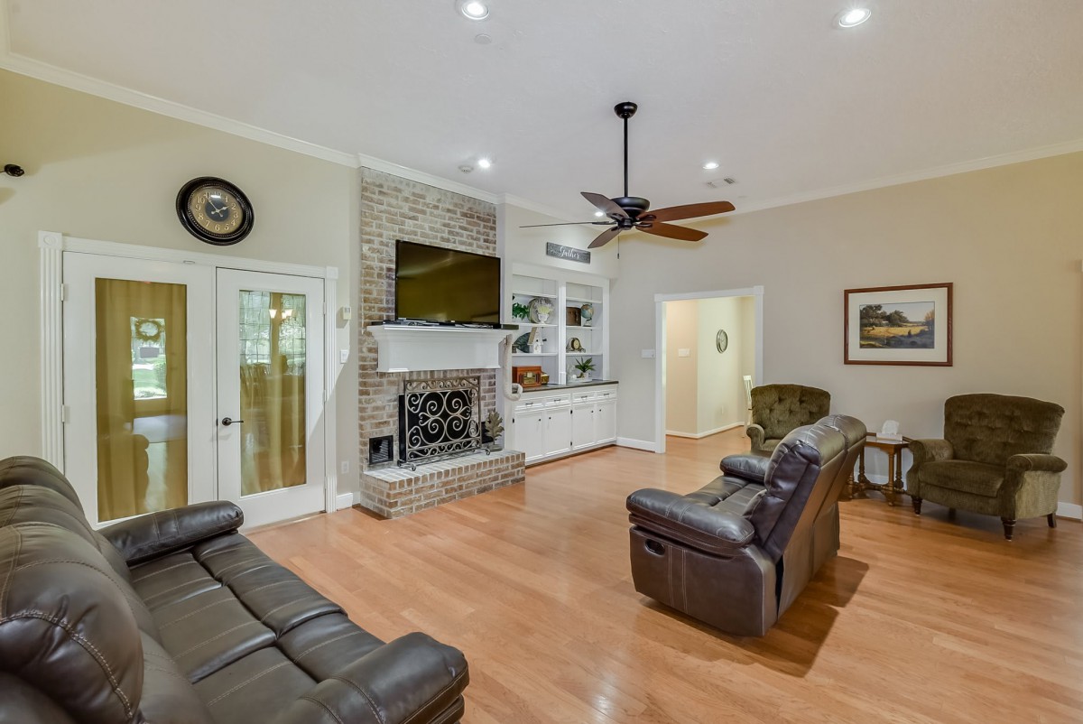 A cozy living room featuring leather sofas, a stone fireplace with a mounted TV, and hardwood flooring.