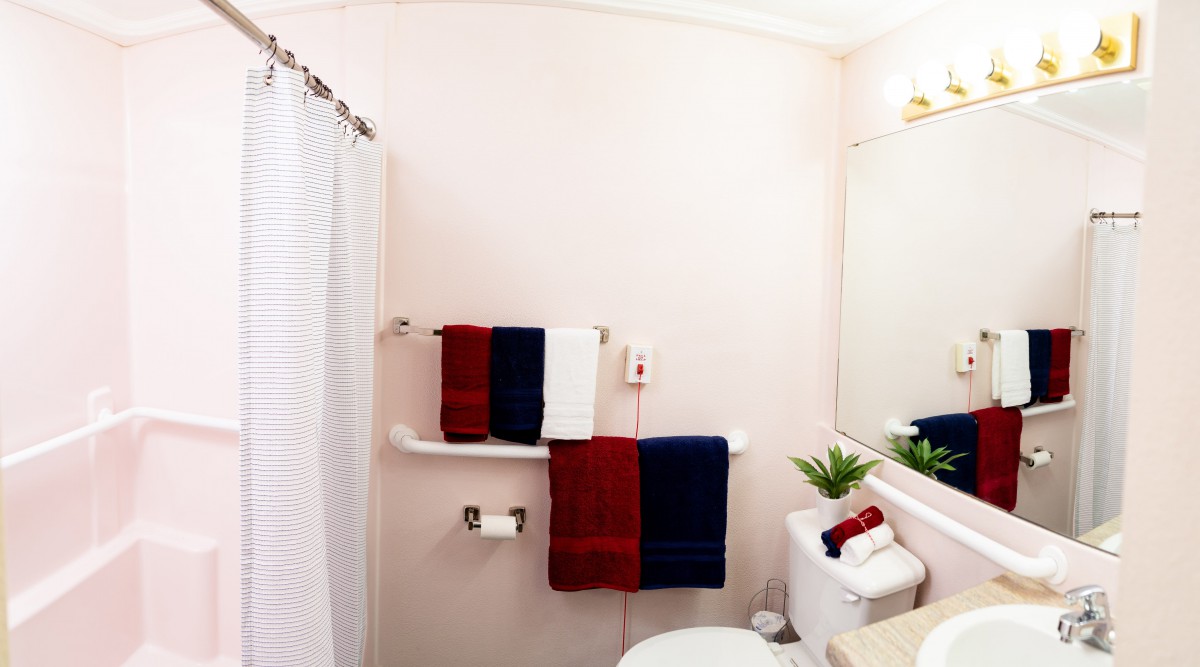 A neatly organized bathroom with red, white, and blue towels hanging on a rack, a sink with a mirror above it, and a white shower curtain.