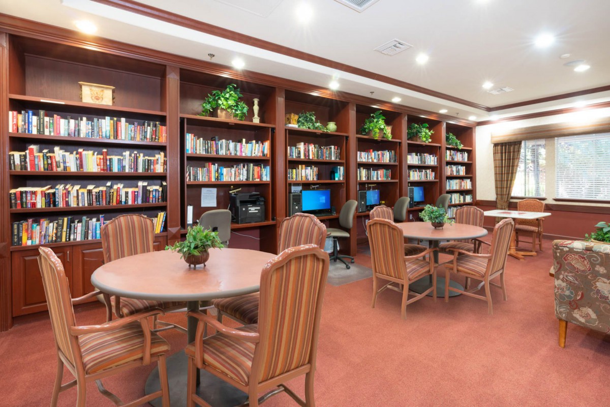 A cozy library space with shelves full of books, tables and chairs for reading, and computers for digital access.