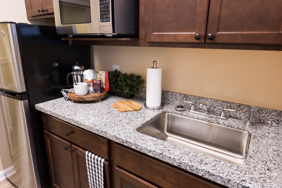 A modern kitchen countertop with a sink, microwave, and various items including a coffee maker and cutting board.