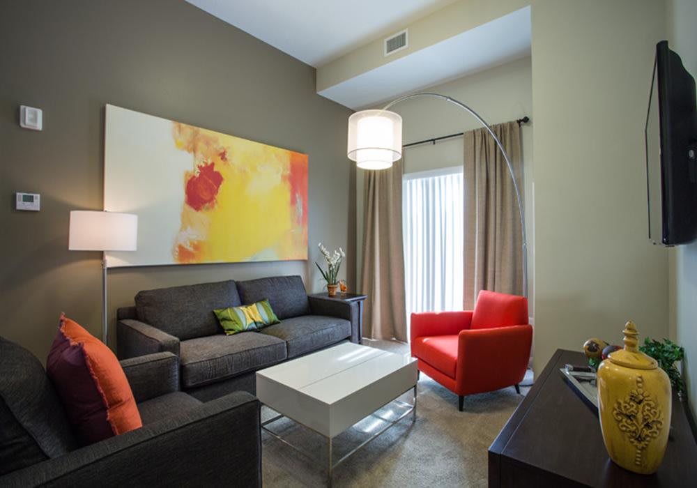 A modern living room featuring a dark gray sofa, a bright red armchair, and a white coffee table, accented by colorful abstract artwork on the wall.