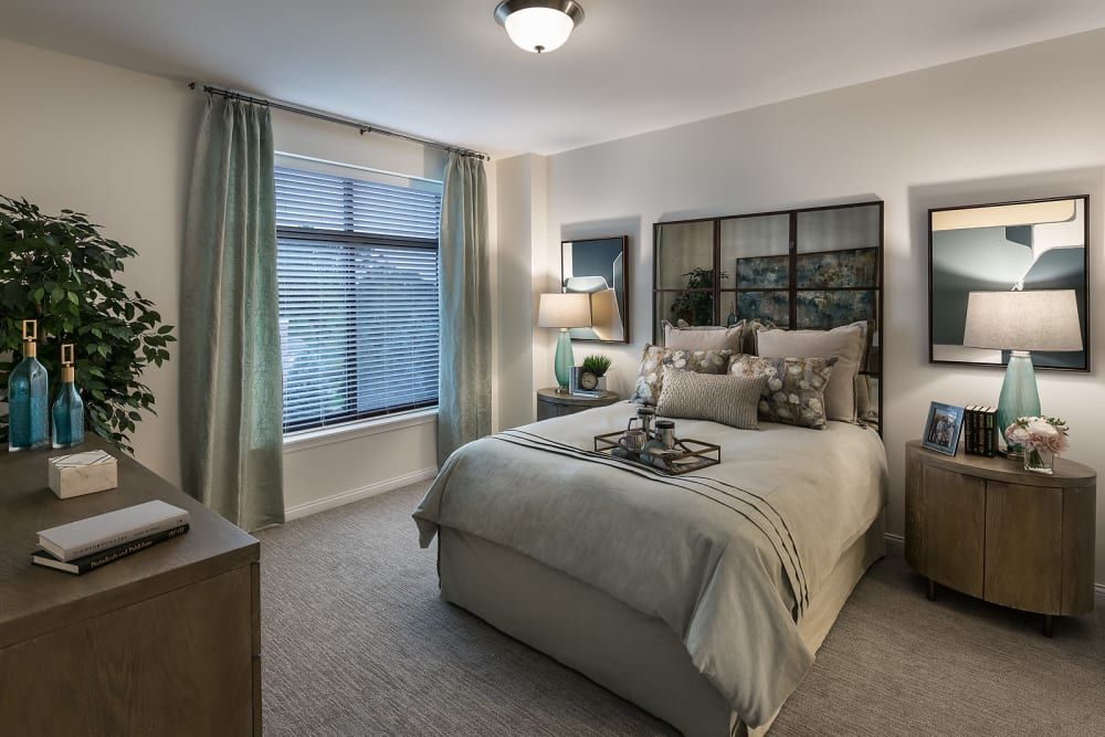 A cozy and modern bedroom featuring a neatly made bed with decorative pillows, a bedside lamp, and large window drapes.