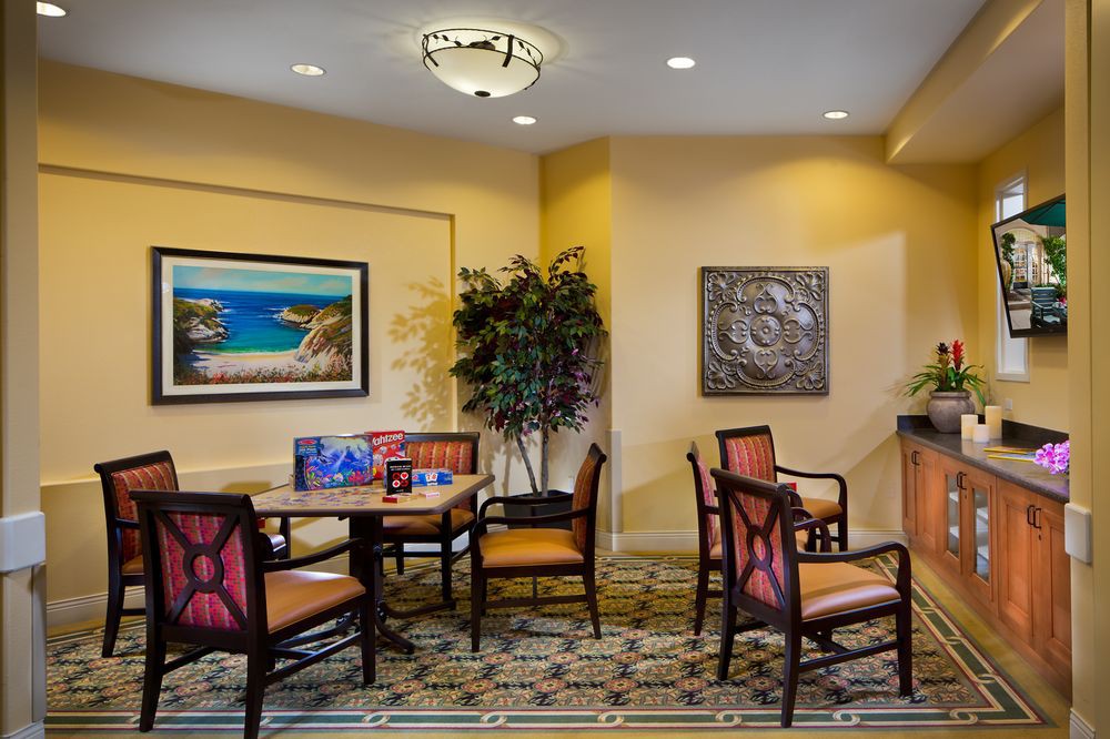 A cozy lobby seating area with chairs, tables, wall art, and a potted plant.